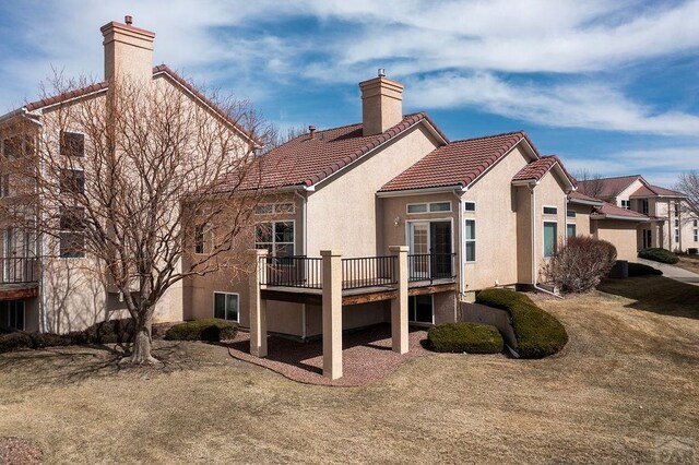 rear view of house featuring a residential view, stucco siding, a tiled roof, and a chimney