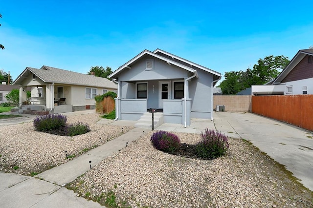 bungalow-style home with covered porch, fence, and stucco siding