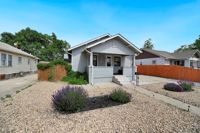 view of front of home with covered porch, fence, and stucco siding