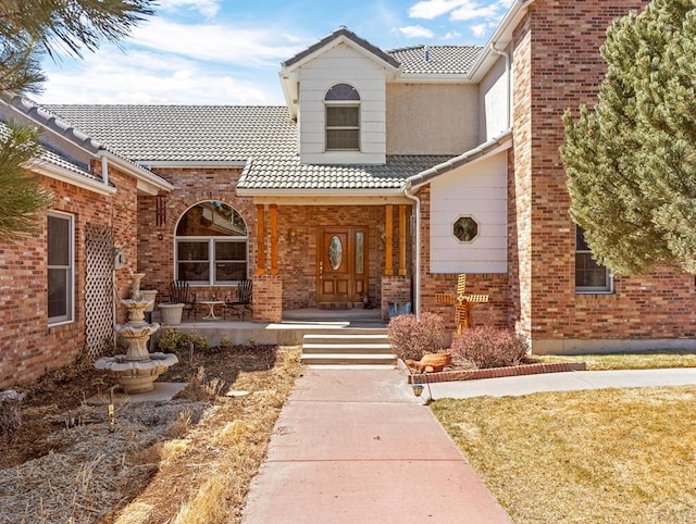 view of front of house featuring a tiled roof, brick siding, and a porch