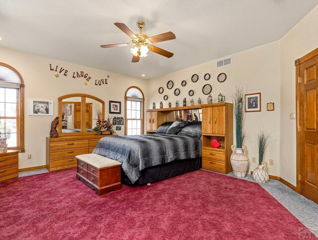 carpeted bedroom featuring baseboards, multiple windows, visible vents, and ceiling fan