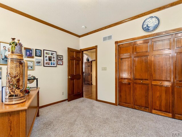 bedroom with crown molding, baseboards, visible vents, and light colored carpet