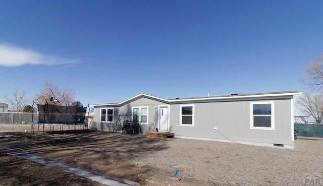 rear view of property featuring crawl space, a trampoline, and fence