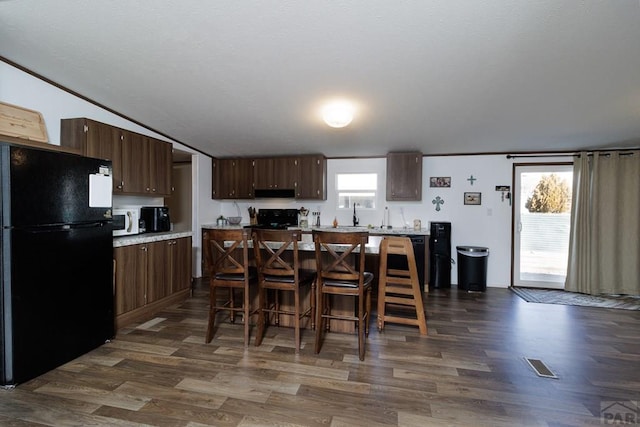 kitchen featuring dark wood-style flooring, white microwave, freestanding refrigerator, under cabinet range hood, and a kitchen breakfast bar