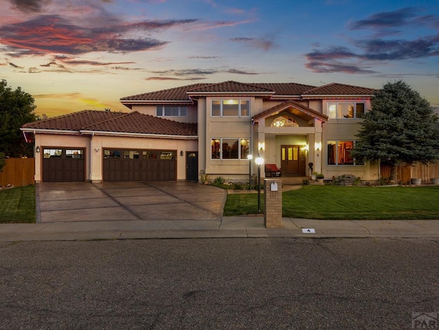 mediterranean / spanish house with concrete driveway, a lawn, a tile roof, an attached garage, and stucco siding