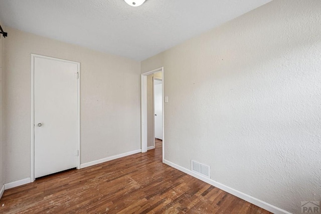 empty room with baseboards, visible vents, and wood finished floors