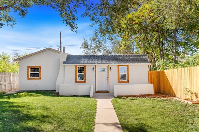 view of front of property with a shingled roof, a front yard, a fenced backyard, and stucco siding