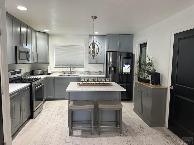 kitchen with light wood-style flooring, a kitchen island, stainless steel appliances, light countertops, and a sink