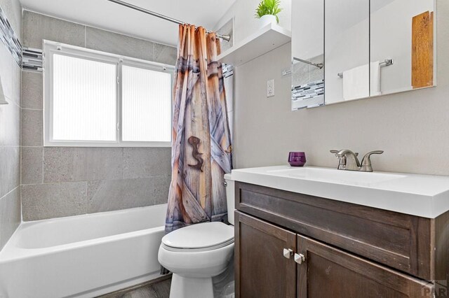 full bath with toilet, wood finished floors, shower / bath combination with curtain, and vanity