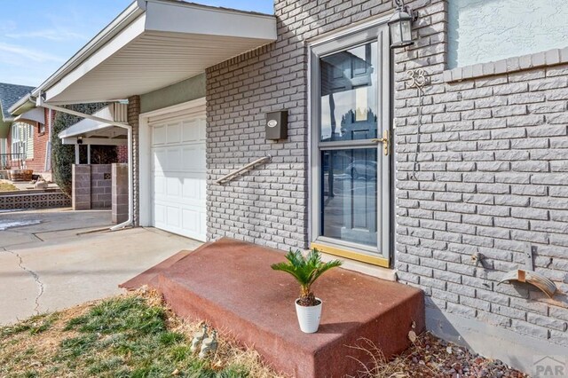 doorway to property featuring a garage, driveway, and brick siding