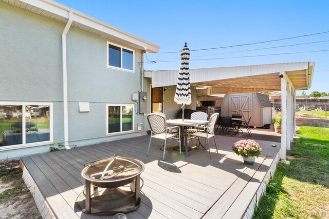 deck featuring outdoor dining space, an outdoor fire pit, a storage unit, and an outdoor structure