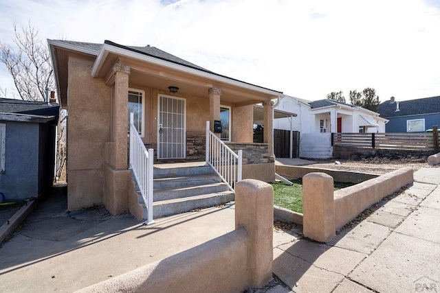 view of front of house featuring stone siding, covered porch, fence, and stucco siding