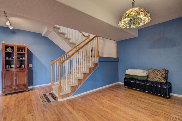 stairs with wood finished floors, rail lighting, and baseboards