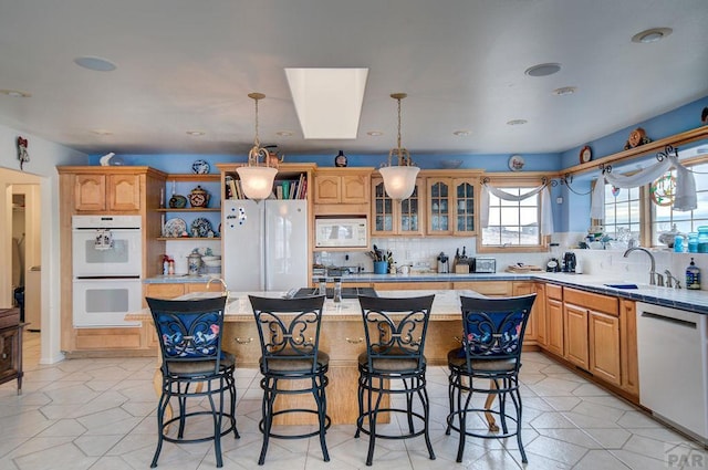 kitchen with white appliances, a sink, a kitchen island, hanging light fixtures, and glass insert cabinets