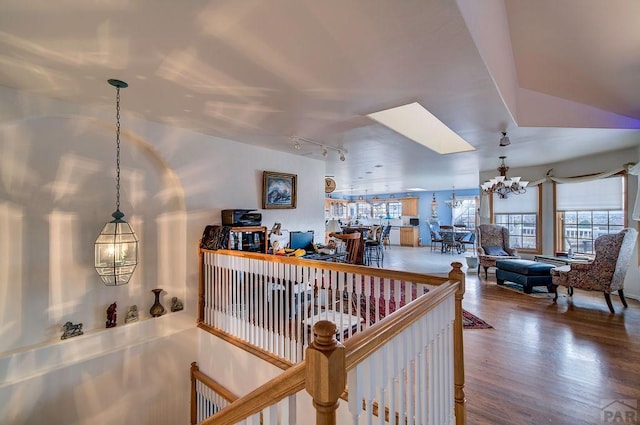 hallway with rail lighting, wood finished floors, a notable chandelier, and an upstairs landing