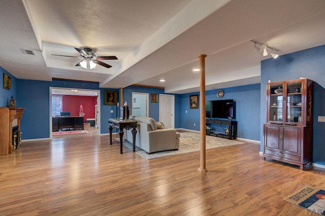 living room featuring baseboards, visible vents, wood finished floors, a textured ceiling, and a fireplace