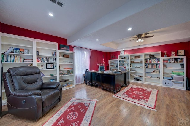 office area with a tray ceiling, light wood-type flooring, visible vents, and recessed lighting