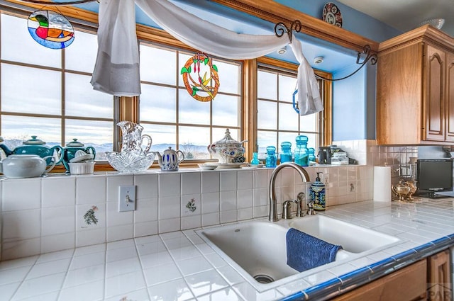 kitchen featuring brown cabinetry, a sink, tile countertops, and decorative backsplash