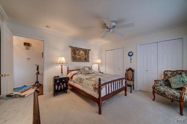 bedroom with light carpet, crown molding, a ceiling fan, and two closets