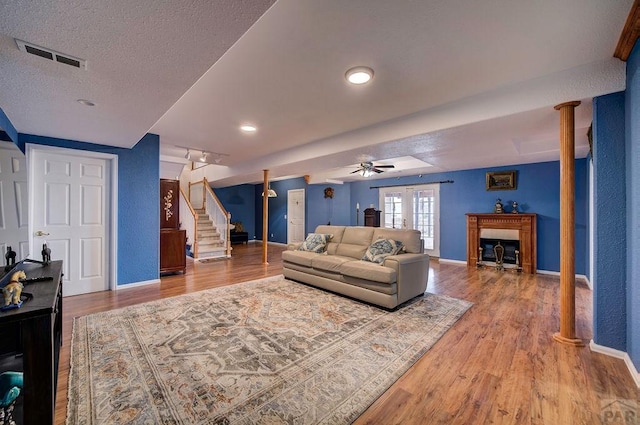 living area with a textured ceiling, a fireplace, wood finished floors, visible vents, and stairs