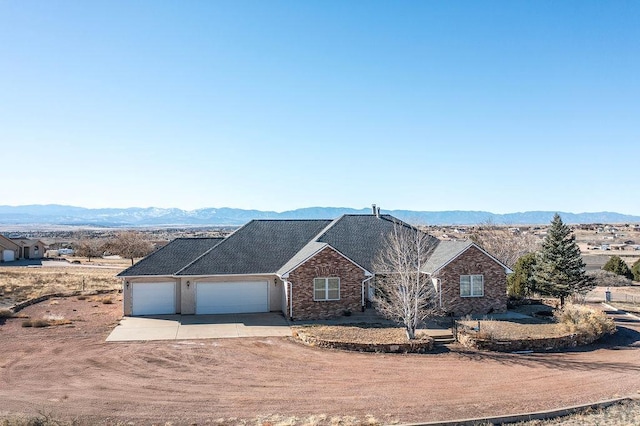 single story home featuring concrete driveway, roof with shingles, a mountain view, and an attached garage