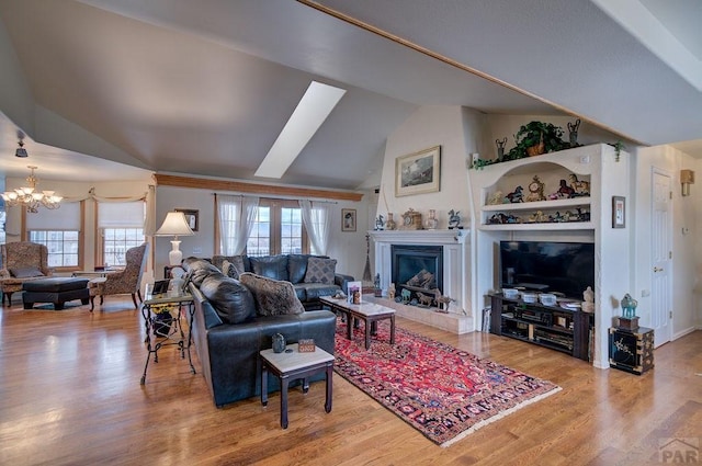 living room with vaulted ceiling, a glass covered fireplace, wood finished floors, and an inviting chandelier