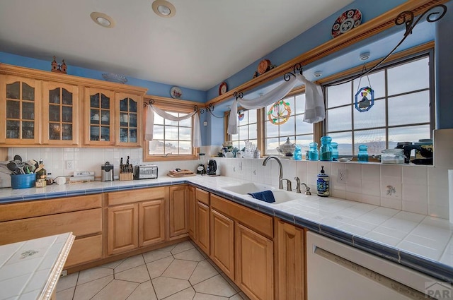 kitchen featuring tile countertops, a sink, glass insert cabinets, and dishwasher