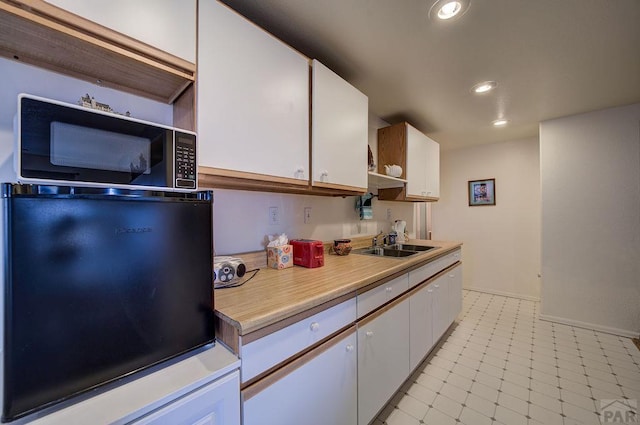 kitchen featuring light countertops, white cabinets, a sink, and fridge