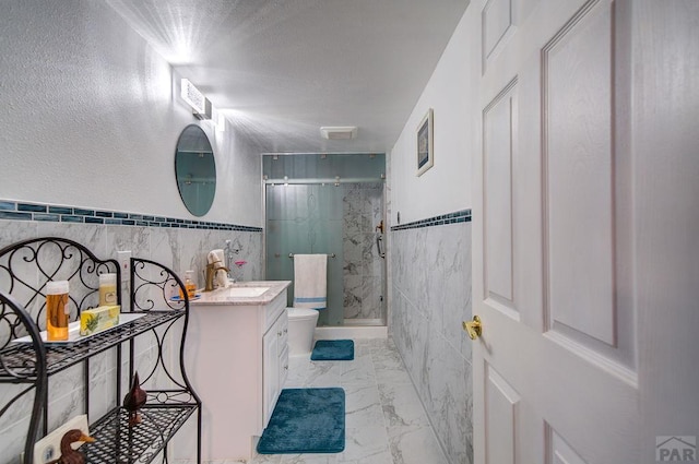 full bathroom featuring marble finish floor, tile walls, toilet, a stall shower, and vanity