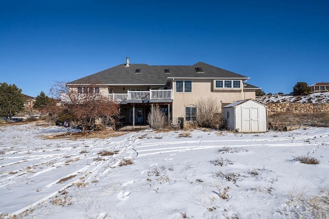 snow covered house with a balcony, stucco siding, a shed, and an outbuilding