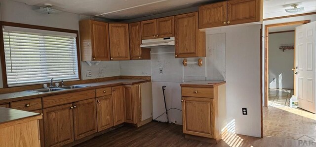 kitchen with under cabinet range hood, dark wood-type flooring, a sink, light countertops, and brown cabinetry