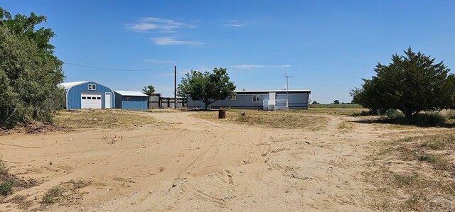 view of yard with dirt driveway, a detached garage, and an outbuilding