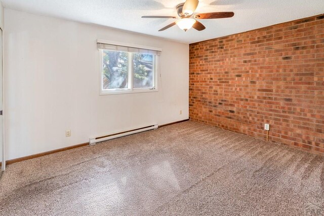 carpeted empty room featuring a textured ceiling, ceiling fan, a baseboard heating unit, brick wall, and baseboards