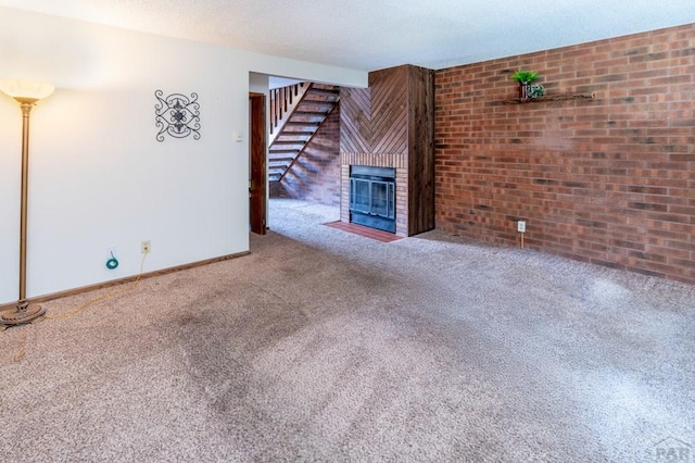 unfurnished living room with carpet floors, a fireplace, stairway, brick wall, and baseboards