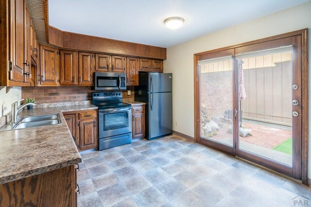 kitchen featuring brown cabinets, stainless steel appliances, decorative backsplash, a sink, and baseboards