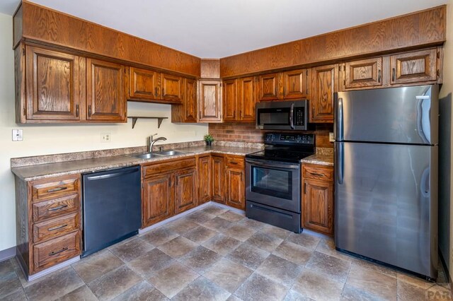 kitchen featuring appliances with stainless steel finishes, stone finish floor, brown cabinetry, and a sink