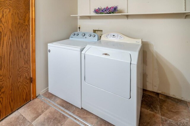 clothes washing area featuring baseboards, laundry area, stone tile flooring, and washer and dryer