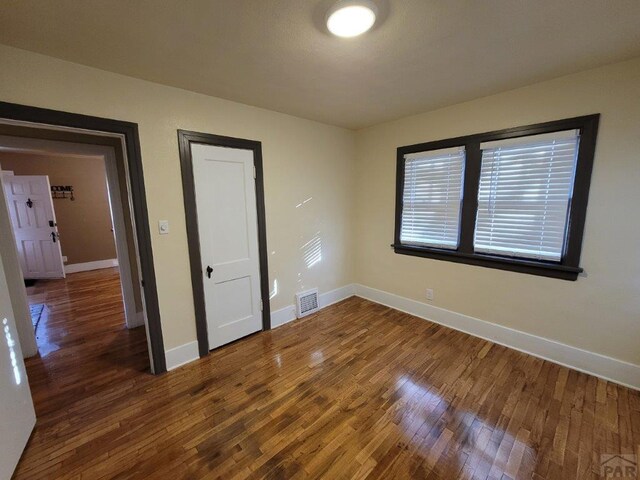 unfurnished bedroom with dark wood-style floors, visible vents, and baseboards