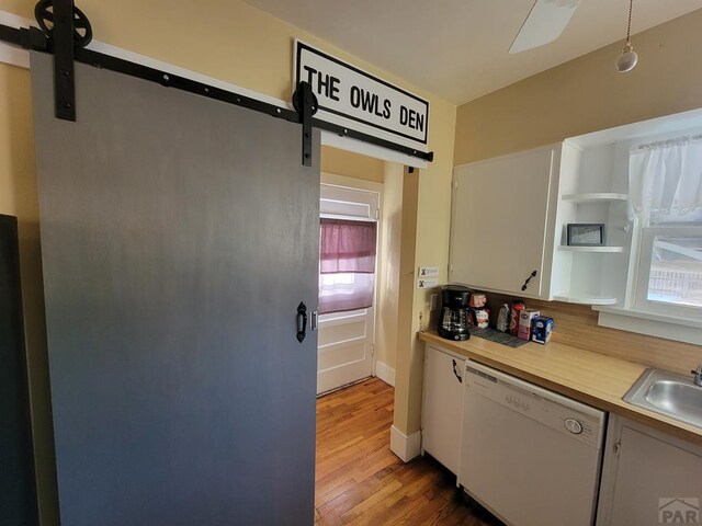 kitchen featuring a barn door, white cabinets, white dishwasher, light countertops, and a sink