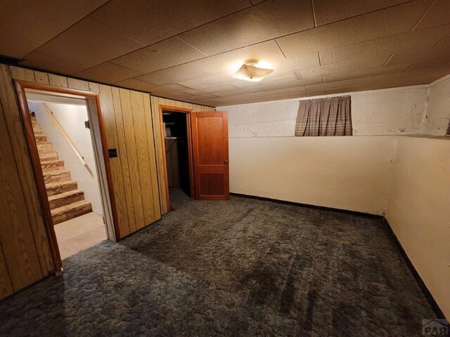 finished basement featuring concrete block wall, stairway, and carpet flooring