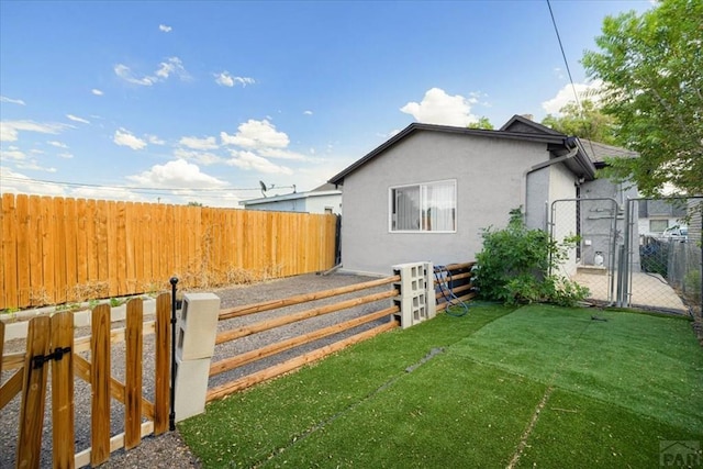 view of side of property with a gate, a yard, a fenced backyard, and stucco siding