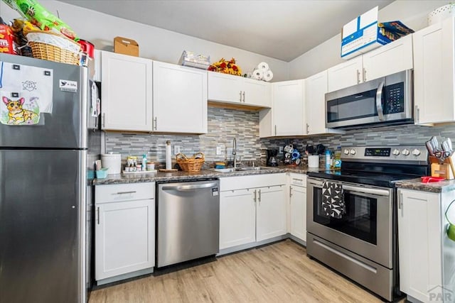 kitchen with a sink, backsplash, white cabinetry, light wood-style floors, and appliances with stainless steel finishes