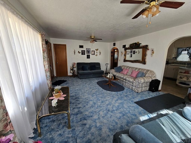 carpeted living area featuring a textured ceiling, arched walkways, and ceiling fan