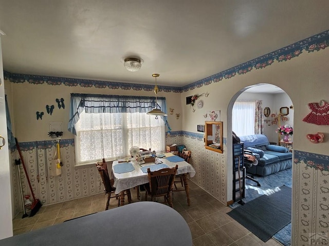 dining area featuring arched walkways, wainscoting, tile patterned flooring, and wallpapered walls