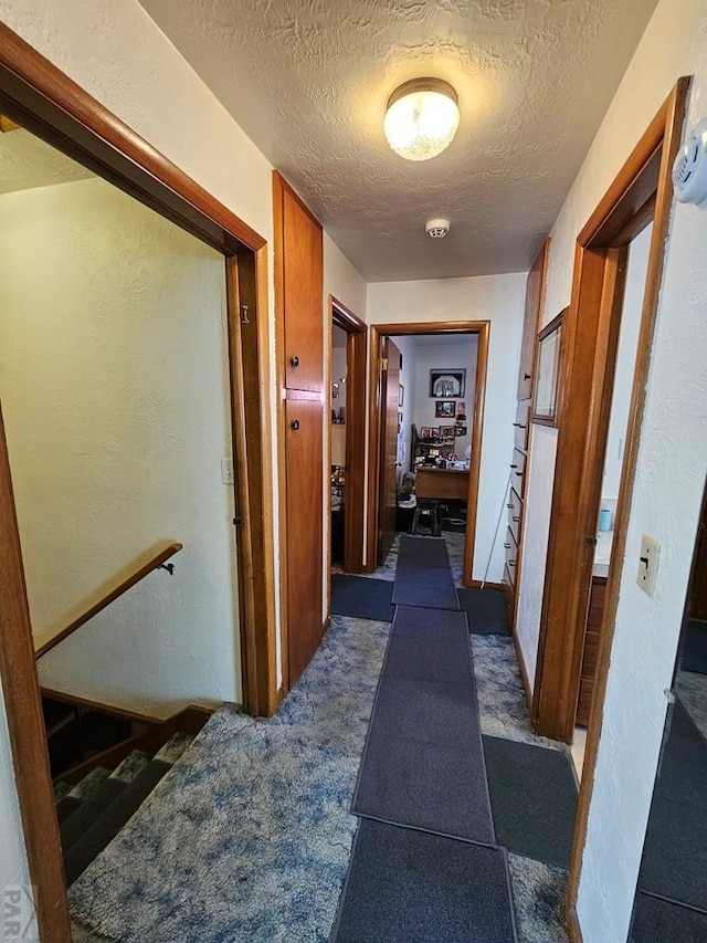 hall with a textured ceiling and a textured wall