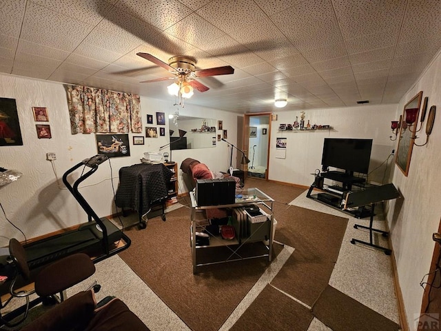 exercise room featuring baseboards, carpet flooring, a paneled ceiling, ceiling fan, and a textured wall