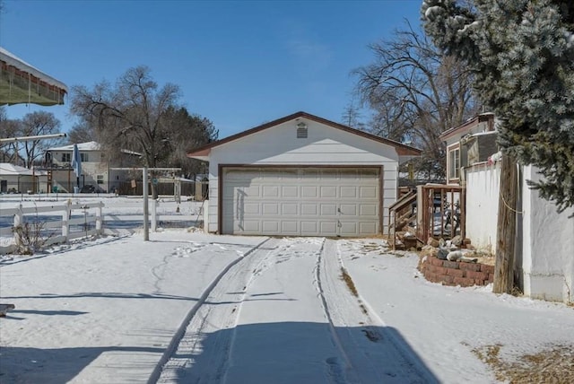 snow covered garage featuring fence and a detached garage