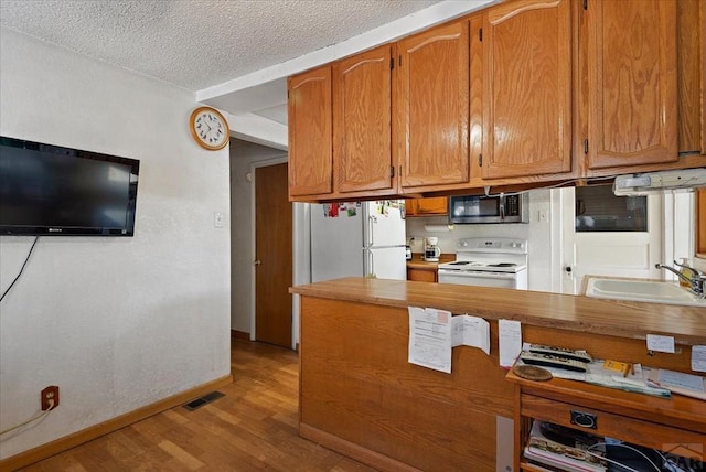 kitchen featuring light countertops, light wood-style flooring, brown cabinetry, a sink, and white appliances