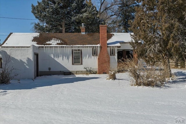 snow covered rear of property featuring a chimney