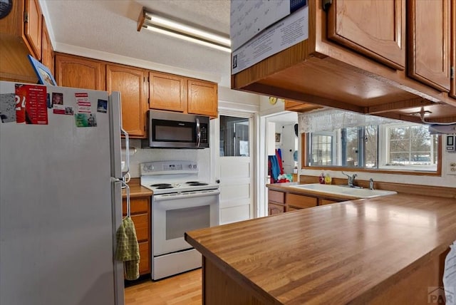 kitchen featuring light wood-style floors, appliances with stainless steel finishes, brown cabinets, and a sink